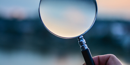 Image of a hand holding a magnifying glass 